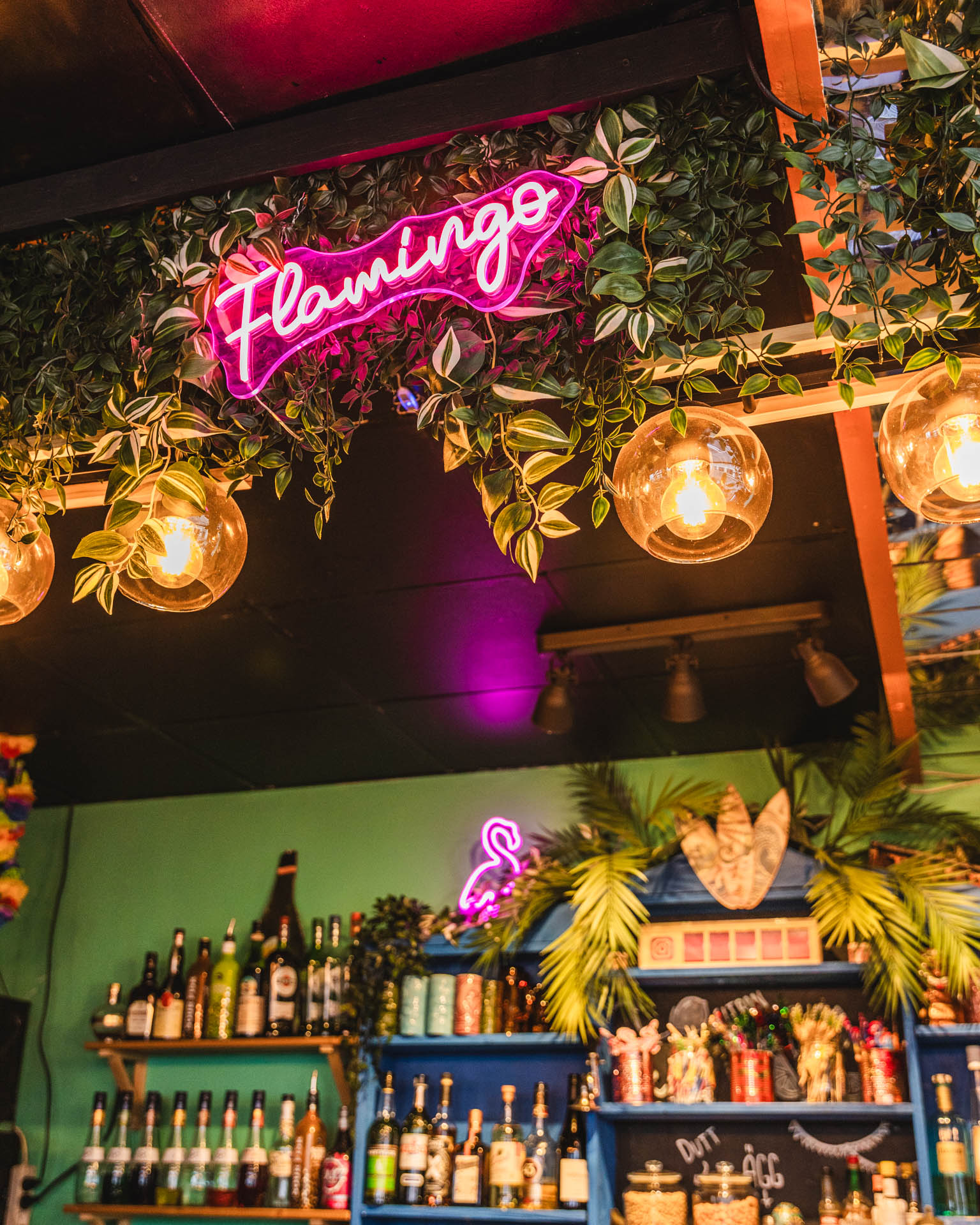 Flamingo Bars interiör med rosa neonskylt, hängande växter och välfylld bardisk